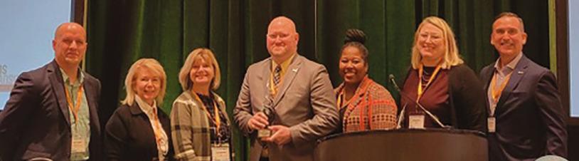 TARTA Chief Customer Experience and Mobility Officer Rick Bailey, center, with the OPTA Collaborative Excellence Award. He was joined on stage by Destination Toledo President and CEO Lance Woodworth, TARTA CEO Laura Koprowski, and TARTA Trustees Mary Morrison, Kendra Smith and Brittany Ford.